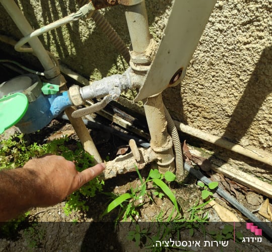 יד מצביעה על צינור מים חלוד עם ברז